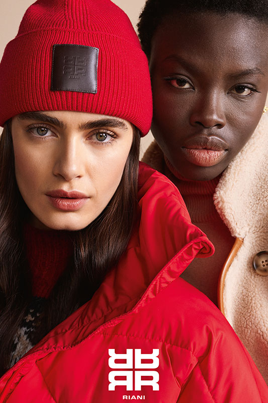 Zwei Frau, die eine in einem beigen Mantel, die andere mit roter Mütze und rotem Mantel